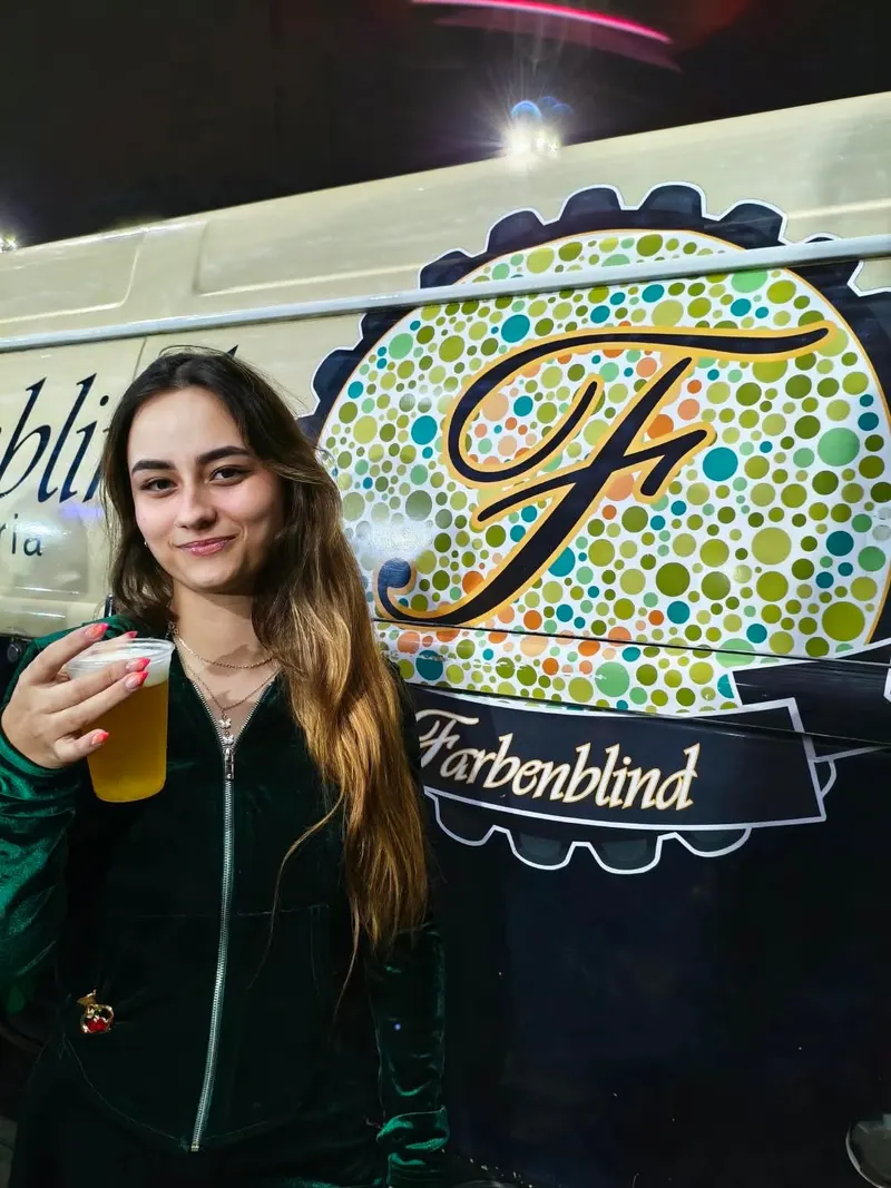 Convidada com um copo de chopp em frente ao logo de bolinhas da Kombeer, na Feira da Lua